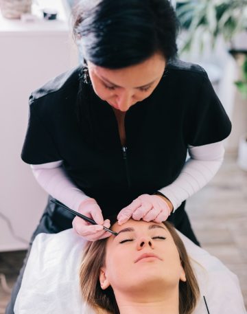 Beautician styling eyebrow shape and design on her client's face in a beauty salon