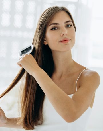 Brushing hair. Portrait of young woman brushing straight natural hair with comb.