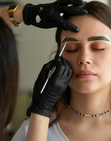 The process of dyeing the eyebrows of a young brunette by an eyebrow master with a brush with paint