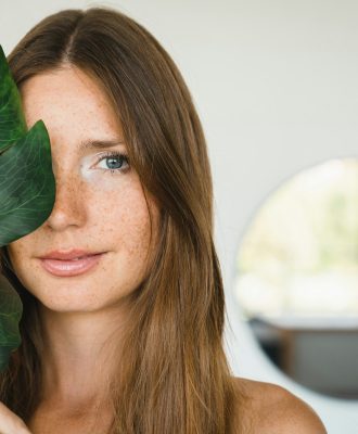 Young beautiful woman covering her face with green leaf at home. Beauty and skin care concept